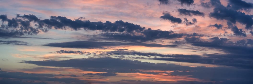 Panoramic view of the vast sky, dominated by a variety of clouds, hints of pink and blue suggest the interplay of the setting or rising sun, creating a soothing, calm atmosphere