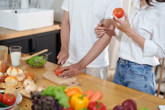 Couple cutting tomatoes for cooking or salad in home kitchen.