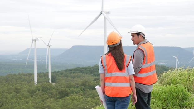 Male and female engineers working on a wind farm atop a hill or mountain in the rural. Progressive ideal for the future production of renewable, sustainable energy.