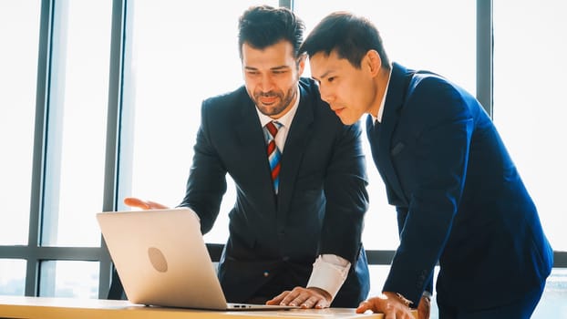 Two business people talk project strategy at office meeting room. Businessman discuss project planning with colleague at modern workplace while having conversation and advice on financial report. Jivy