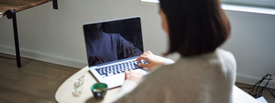 Rear view of woman, typing and working on laptop, computer screen is empty for copy space, female student studying remotely.