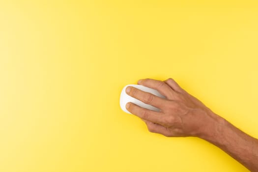 First person top view photo of black male hand with white computer wireless mouse on isolated yellow background with copyspace