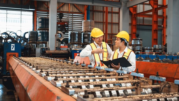 Factory worker operating metal stamping machine while supervised by engineer for optimal quality output of industrial goods on assembly steel forming line in heavy industry factory. Exemplifying