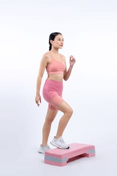 Vigorous energetic woman doing exercise at on studio short isolated background with cardio aerobic step workout. Young athletic asian woman dexterity and endurance training session concept.