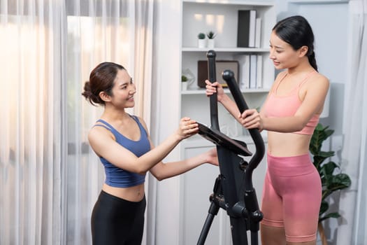 Energetic and strong athletic asian woman running on elliptical running machine at home with workout buddy or trainer. Pursuit of fit physique and commitment to healthy lifestyle. Vigorous