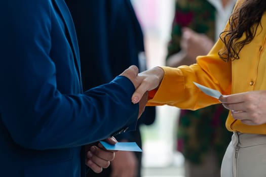 Businessmen shaking hand and making a contract in the sign of agreement, cooperation with businesswoman. Cropped image of managers holding business cards. Their partners standing behind. Intellectual.