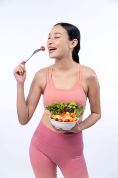 Young sporty Asian woman in sportswear holding salad bowl fill with vibrant of fruit and vegetable. Natural youthful and fit body lifestyle with balance nutrition on isolated background. Vigorous