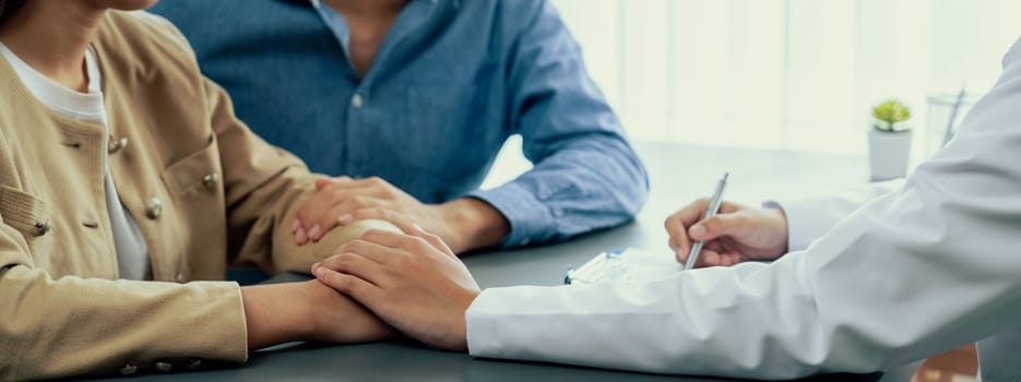 Doctor providing compassionate healthcare consultation while young couple patient holding hand, comfort each other after infertile report. Reproductive and medical fertility consulting. Neoteric