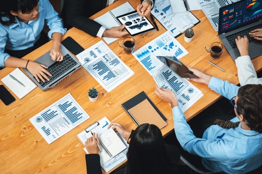 Wide top view of diverse group of business analyst team analyzing financial data report paper on meeting table. Chart and graph dashboard by business intelligence analysis. Meticulous