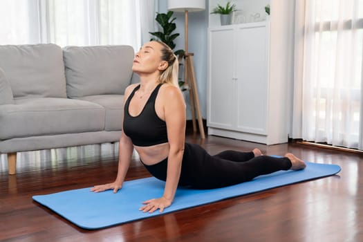 Senior woman in sportswear being doing yoga in meditation posture on exercising mat at home. Healthy senior pensioner lifestyle with peaceful mind and serenity. Clout