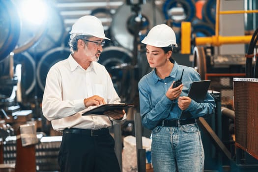 Factory engineer manager with assistant using laptop to conduct inspection of steel industrial machine, exemplifying leadership as machinery engineering inspection supervisor in metalwork manufacture.