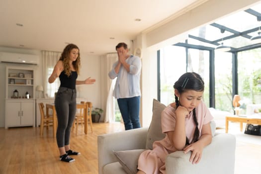 Annoyed and unhappy young girl sitting on sofa trapped in middle of tension by her parent argument in living room. Unhealthy domestic lifestyle and traumatic childhood develop to depression.Synchronos