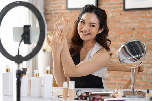 Asian Woman influencer shoot live streaming vlog video review makeup uttermost social media or blog. Happy young girl with cosmetics studio lighting for marketing recording session broadcasting online