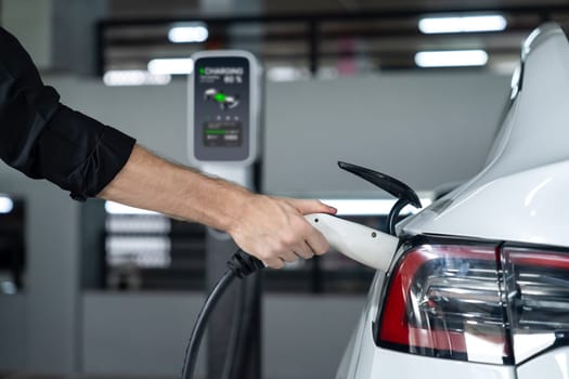 Young man travel with EV electric car to shopping center parking lot charging in downtown city showing urban sustainability lifestyle by green clean rechargeable energy of electric vehicle innards