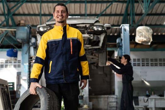 Confident and happy mechanic portrait with smile and wearing uniform standing on automotive service workshop with car lifted on vehicle inspection station background. Oxus