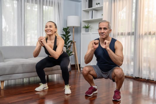 Athletic and sporty senior couple engaging in leg day training session with squat together at home exercise as concept of healthy fit body lifestyle after retirement. Clout