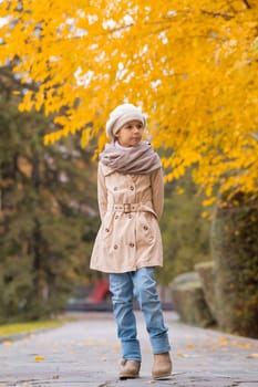 Caucasian girl in a beige coat and beret walks in the park in autumn