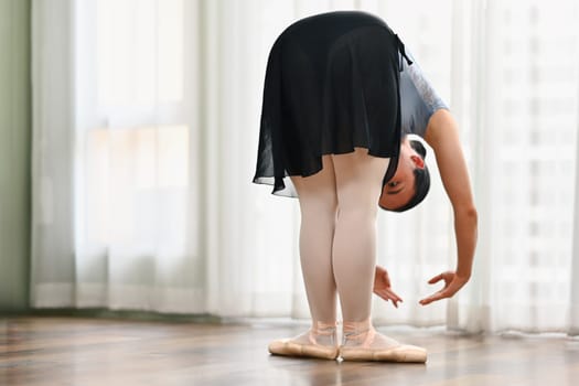 Young ballerina practice ballet near window in dance class. Dance, art, education and flexibility concept.