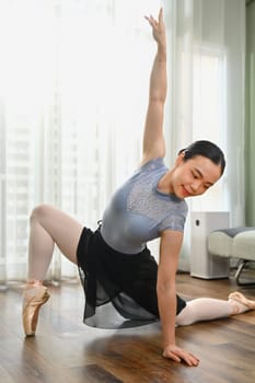 Dedicated young asian woman practicing ballet in bright living room. Dance, art, education and flexibility concept.