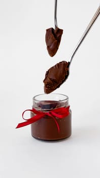 Decadent chocolate spread in jar with red ribbon and spoonfuls.