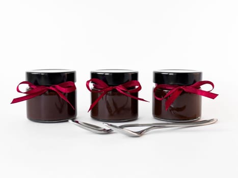 Elegant chocolate jars with red ribbons and silver spoons on white background.