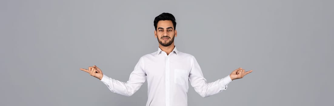 A young Arab businessman stands confidently in a studio, with arms outstretched and a warm smile. He embodies a professional millennial lifestyle focused on entrepreneurship, panorama