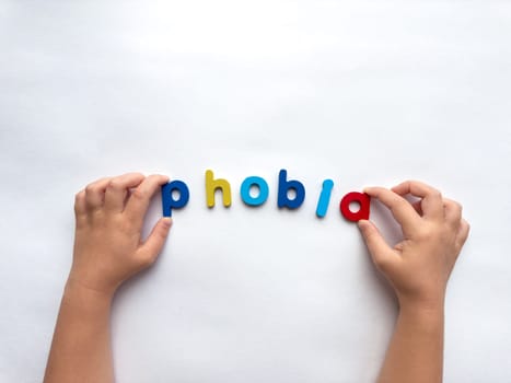 Childs hands spelling phobia with colorful letters on white background.