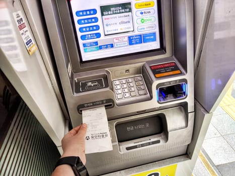 Seoul, Republic of Korea - November 01, 2024: User withdrawing money from an ATM machine in Seoul's bustling urban environment