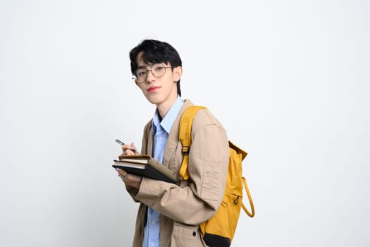 Portrait of male college student with glasses and backpack standing over white background.