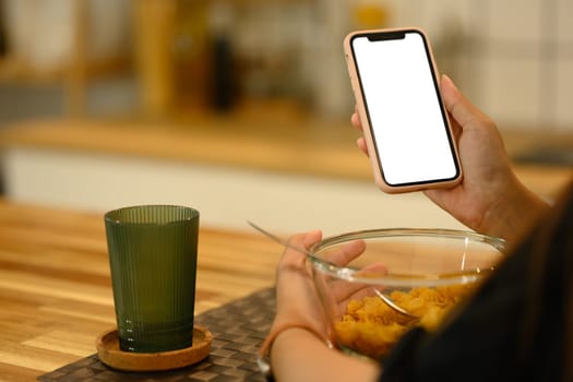 Close up shot woman using her smartphone while having breakfast on kitchen counter.