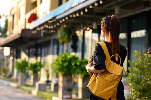 Young woman tourist with yellow backpack walking through a city street at daytime.