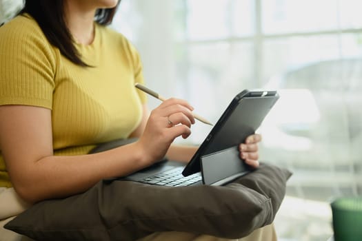 Beautiful young woman in casual clothing using digital tablet on couch in bright living room.