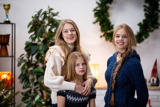 Three sisters happily pose together in cozy and comfortable outfits, all set against a cheerful festive backdrop