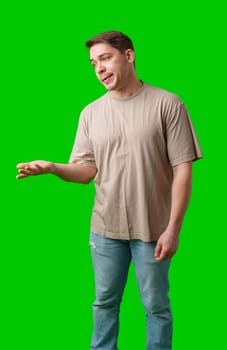 Man with a confused expression gestures with his hands against a bright green background in studio