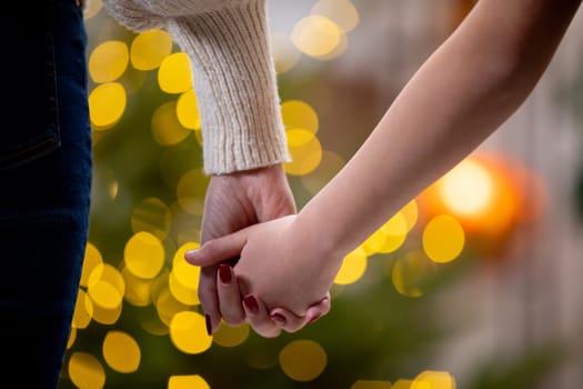 A couple gently holds hands, surrounded by enchanting festive bokeh lights in a beautifully romantic moment