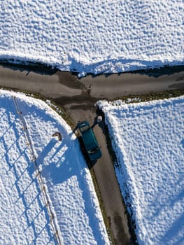 Aerial view of a green car parked near a snowy crossroads in the countryside of Monte Lama, Morfasso, Italy, featuring a wooden fence and melting snow