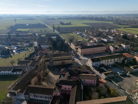 Aerial view of Stagno Lombardo, a small town in the province of Cremona, Lombardy, Italy, showcasing residential buildings, farmlands, and the surrounding countryside under a clear blue sky