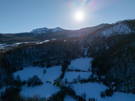 Aerial view of snowy fields and a frozen lake with Monte Lama in the background, near Morfasso, Italy, on a sunny winter day, creating a tranquil and picturesque scene