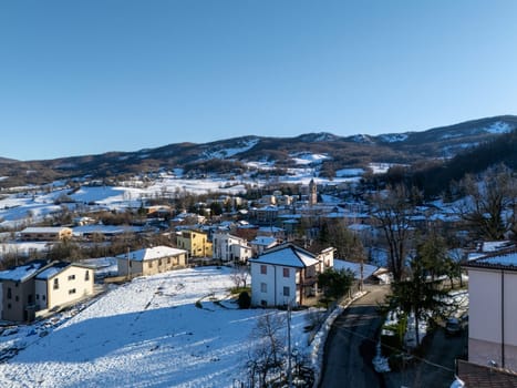 Aerial view capturing Morfasso, a charming village nestled in the Apennine Mountains near Piacenza, blanketed in snow under a bright, sunny winter sky