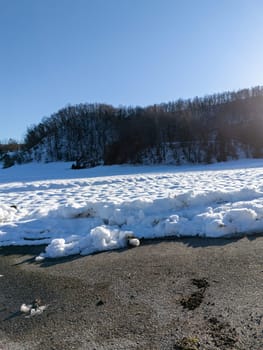 Snow covering the landscape of Monte Lama in Morfasso, Italy, during the winter season, creating a serene and picturesque scene with a clear blue sky and bare trees on the hill