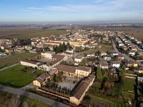 Aerial view of Stagno Lombardo, Italy, showcases residential homes, cultivated farmland, and the town's infrastructure under a clear blue sky