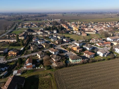 Aerial view of Stagno Lombardo, a small town in the province of Cremona, Lombardy, Italy, showcasing residential buildings, farmlands, and the surrounding countryside under a clear blue sky