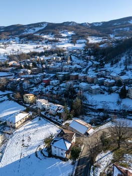 Aerial view of Morfasso, a small village in Emilia Romagna, Northern Italy, covered by snow during winter season, featuring snow-capped roofs, roads and surrounding hills
