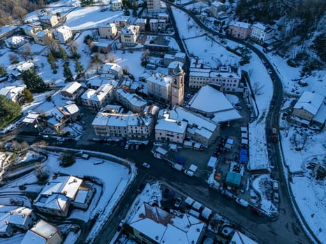 Aerial view of Morfasso, a small village in Emilia Romagna, Northern Italy, covered by snow during winter season, featuring snow-capped roofs, roads and surrounding hills