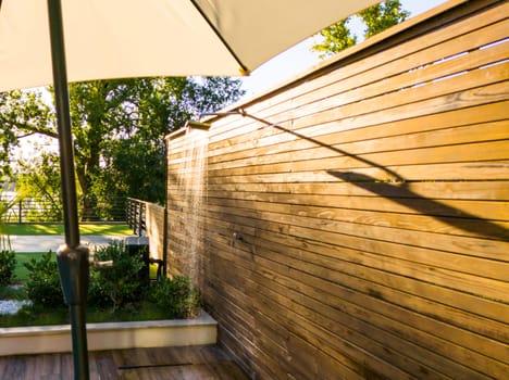 Outdoor shower with wooden privacy fence and umbrella shade in cozy backyard setting