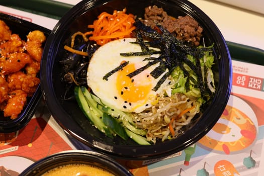 A colorful and vibrant bowl of bibimbap featuring fresh vegetables, tender beef, and a sunnysideup egg atop it