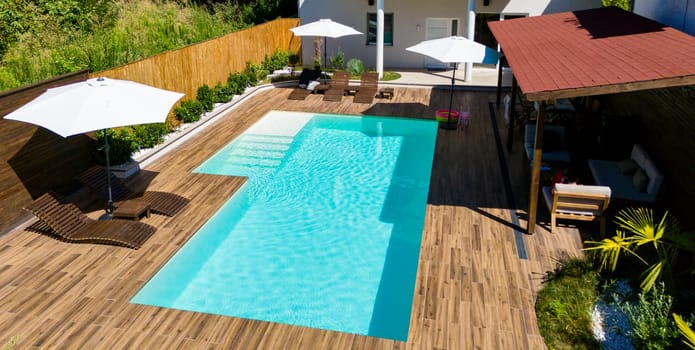 Modern backyard swimming pool with wooden deck, shaded lounge areas, and landscaped greenery