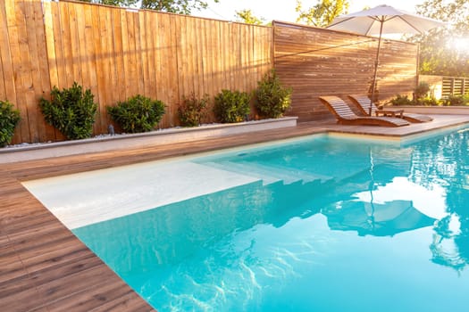 Modern backyard pool with wooden deck and sun loungers. Bright and peaceful outdoor relaxation area with natural sunlight