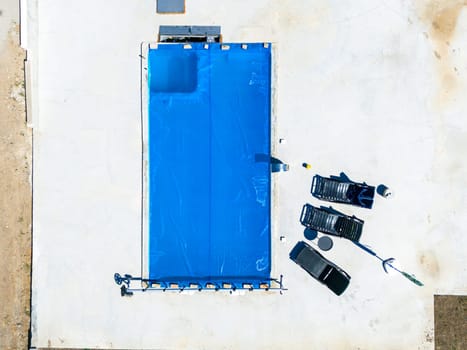 Close-up aerial view of a rectangular pool with a blue cover and construction tools nearby
