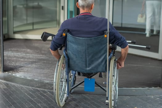Rear view of a person in a wheelchair entering a building through automatic glass doors, urban setting, accessibility concept,
